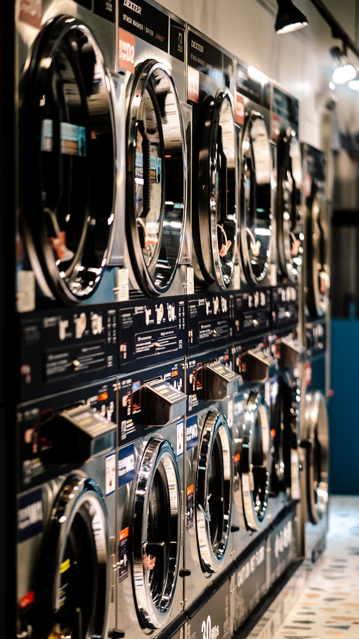 A row of industrial washing machines in a modern laundromat with vibrant lighting.